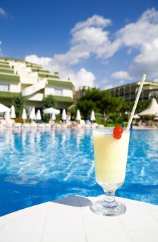 cocktail in glass on a background tourist resort and blue water of pool