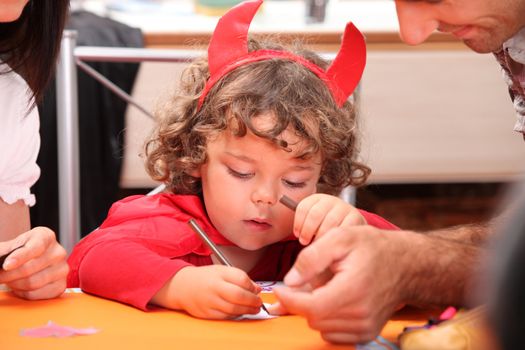 A little kid dressed as the devil drawing.