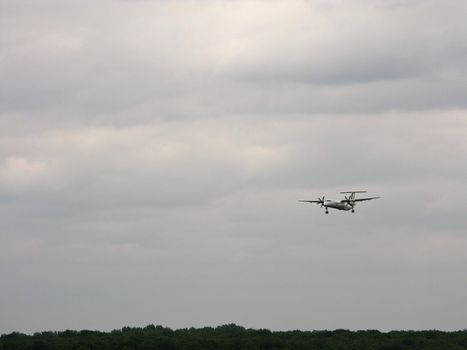 Landing airplane with cloudy sky and forest in background