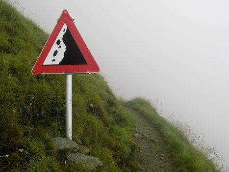 rockfall sign on a hiking path on a steep slope in the alps