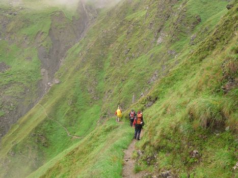 three people on a small path in the alpine mountains walking away from the camera