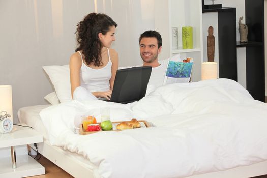 Couple with laptop having breakfast in bed
