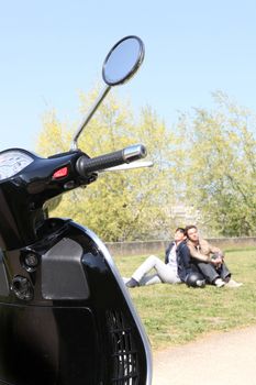 Couple relaxing in a park next to their scooter