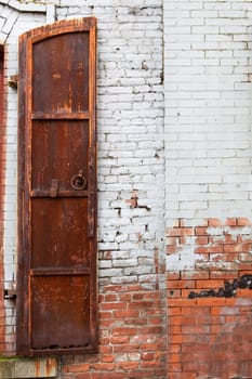 Old weathered and rusted shutter against a white painted red brick wall