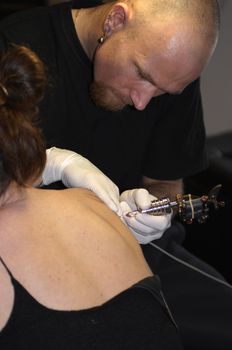 an young artist man tattooing a woman with a professionnal stylet