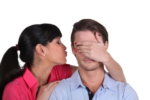 Young woman kissing her boyfriend on the cheek hiding his eyes
