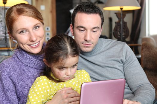 Parents and daughter sat with laptop on sofa