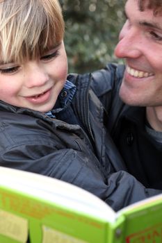 Father and son reading book outdoors