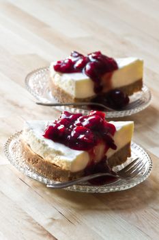 Wooden table with two pieces Mon Chou tart decorated with cherry sauce on glass saucers - vertical image