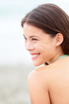 Multiethnic girl portrait on beach. Happy young mixed race woman in bikini smiling joyful outside looking over shoulder. Mixed Asian Chinese / Caucasian female model outside.