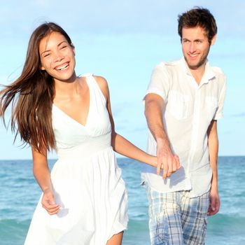 Beach couple walking happy, carefree and joyful on summer vacation. Interracial young couple holding hands. Asian woman, Caucasian man. From Varadero Beach, Cuba.