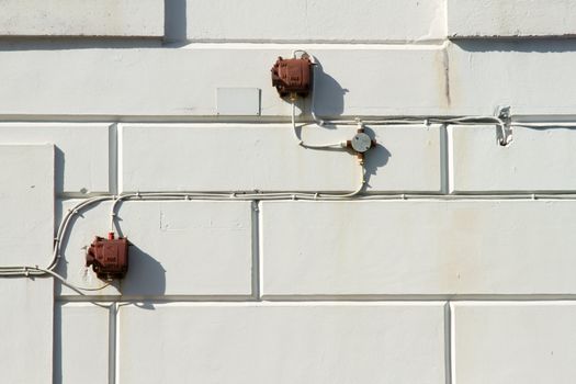 Old outdoor fire switch boxes with cables and a junction box on an external wall with patterned render.