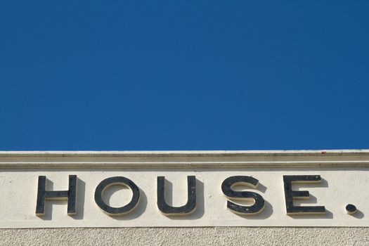 A wall with pebble dash and render with the word 'HOUSE.' on it, against a blue sky.