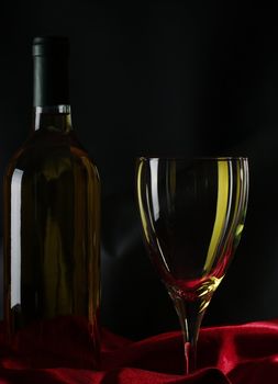 White wine bottle and wine glass on red textile with black background (Selective Focus)