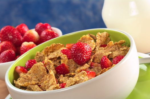 Wholewheat cereal with fresh strawberries in bowl with strawberries and milk in the back (Selective Focus, Focus on the strawberry in the middle) 