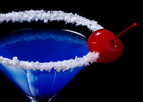 Blue Curacao with coco flakes on the glass rim and garnished with a red maraschino cherry photographed on black (Selective Focus, Focus on the cherry)