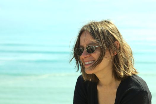 Portrait of a smiling young woman in sunglasses on the coast (Selective Focus, Focus on the left side of the face)