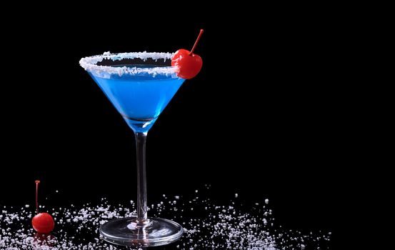 Blue Curacao drink in a glass with coconut flake rim and a maraschino cherry surrounded by coconut flakes and a maraschino cherry photographed on black (Selective Focus, Focus on the front of the glass and the cherry on the rim)