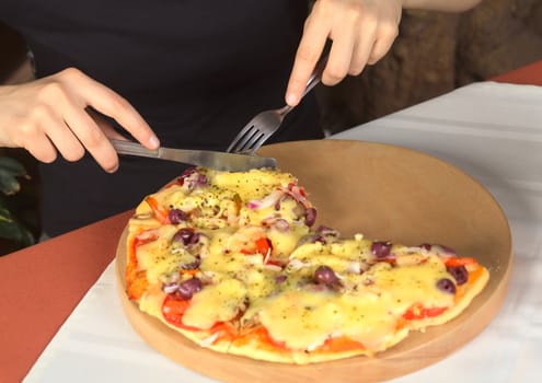 Woman eating vegetarian pizza in a pizzeria (Selective Focus, Focus on the hands, the cutlery and the pizza around the cutlery)