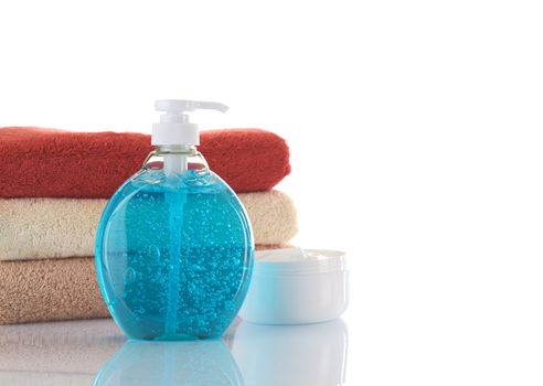 Blue liquid soap with cream and different colored towels in background photographed on white (Selective Focus, Focus on the liquid soap dispenser) 