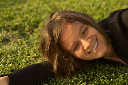 Young Caucasian woman enjoying the evening light in a park lying on the grass (Selective Focus, Focus on the face)