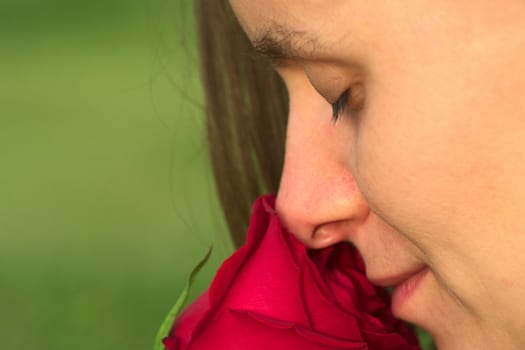Young Caucasian woman smelling at a red rose with closed eyes (Very Shallow Depth of Field) 