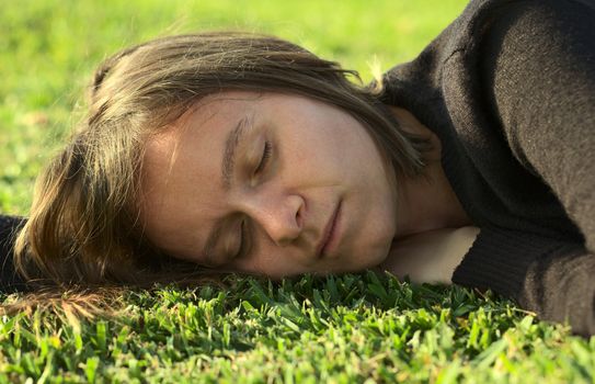 Young Caucasian woman sleeping on grass in a park lit by the evening light (Selective Focus, Focus on the left eye)