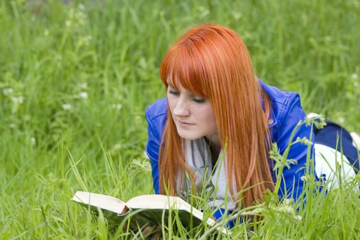 Young beautiful girl with red hair reading a book 