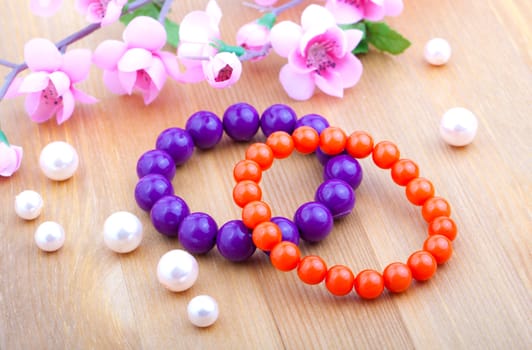 multi color coral bangles and artificial pearls, with pink flower on wooden background