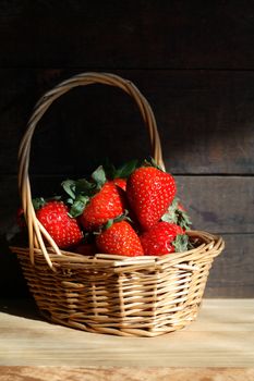 Wicker basket full of strawberries on wooden background under sunbeam