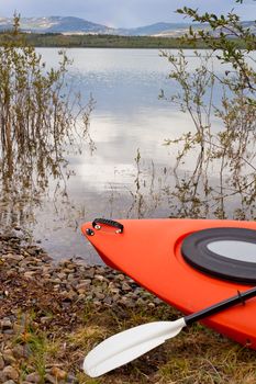 Kayak and paddle beached on the shore alongside a tranquil lake with a mountain range in the distance