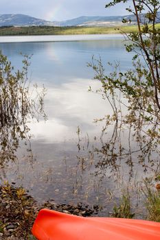 Kayak beached on the shore alongside a tranquil lake with a mountain range in the distance