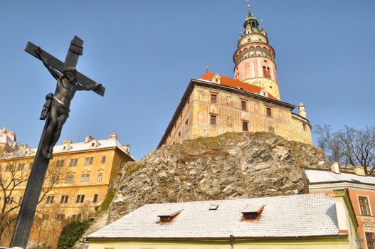 A statue of Jesus Christ crucified against of a castle situated on a cliff. Wintr Krumlov, Czech Republic