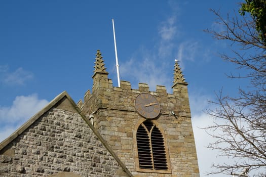 A clock on the tower of a stone built church with a blue sky  and cloud.