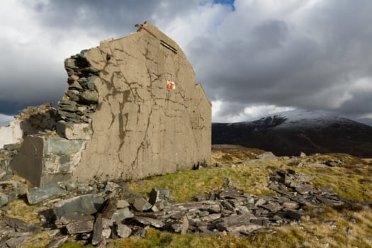 A derelict building with rendered gable end in a rural setting and a mountain in the background.