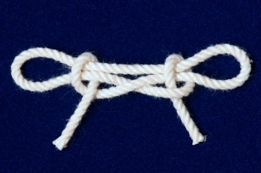 Nautical knot tied in white cord on blue background