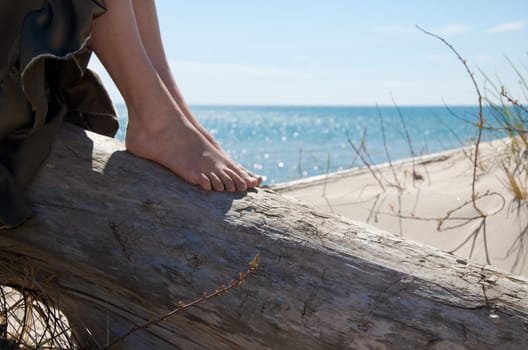 A woman relaxes on a log at a beach.