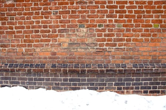 Background of ancient grunge aged red brick wall and snow in winter.