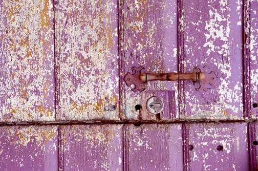 Background of an old painted, crumbled door. Handle on purple wooden planks.