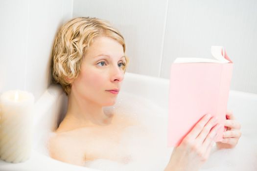 Young woman relaxing and reading in the bath
