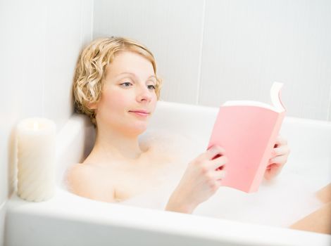 Young woman relaxing and reading a book in the bath with candlelight