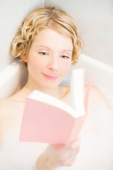 Happy young woman reading a book in the bath