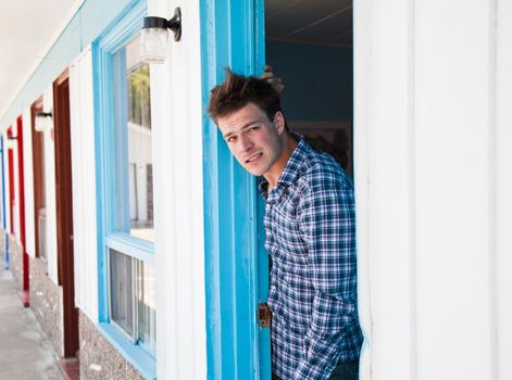 Worried young man looks out of the ugly motel room