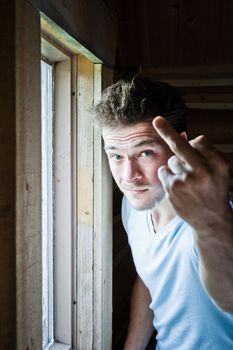 Young man doing a bad gesture at the window frame