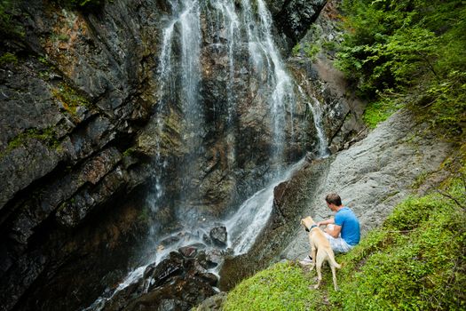 Young man with a dog near a waterfall in the forest