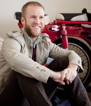 Young beared man sitting next to red and white scooter.