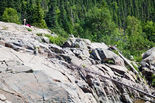 Girl sitting very far on a huge rock