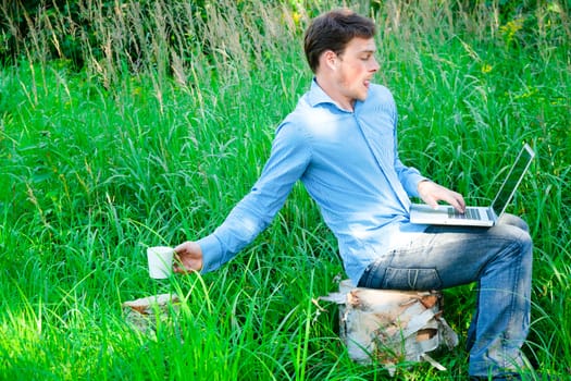 Young man typing outdoors with a cup and laptop