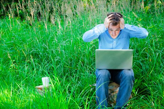 Despaired man outdoors with a cup and laptop