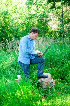 Young man outdoors with a cup and laptop in the forest